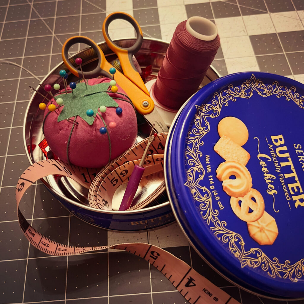 Open blue cookie tin with sewing supplies inside.