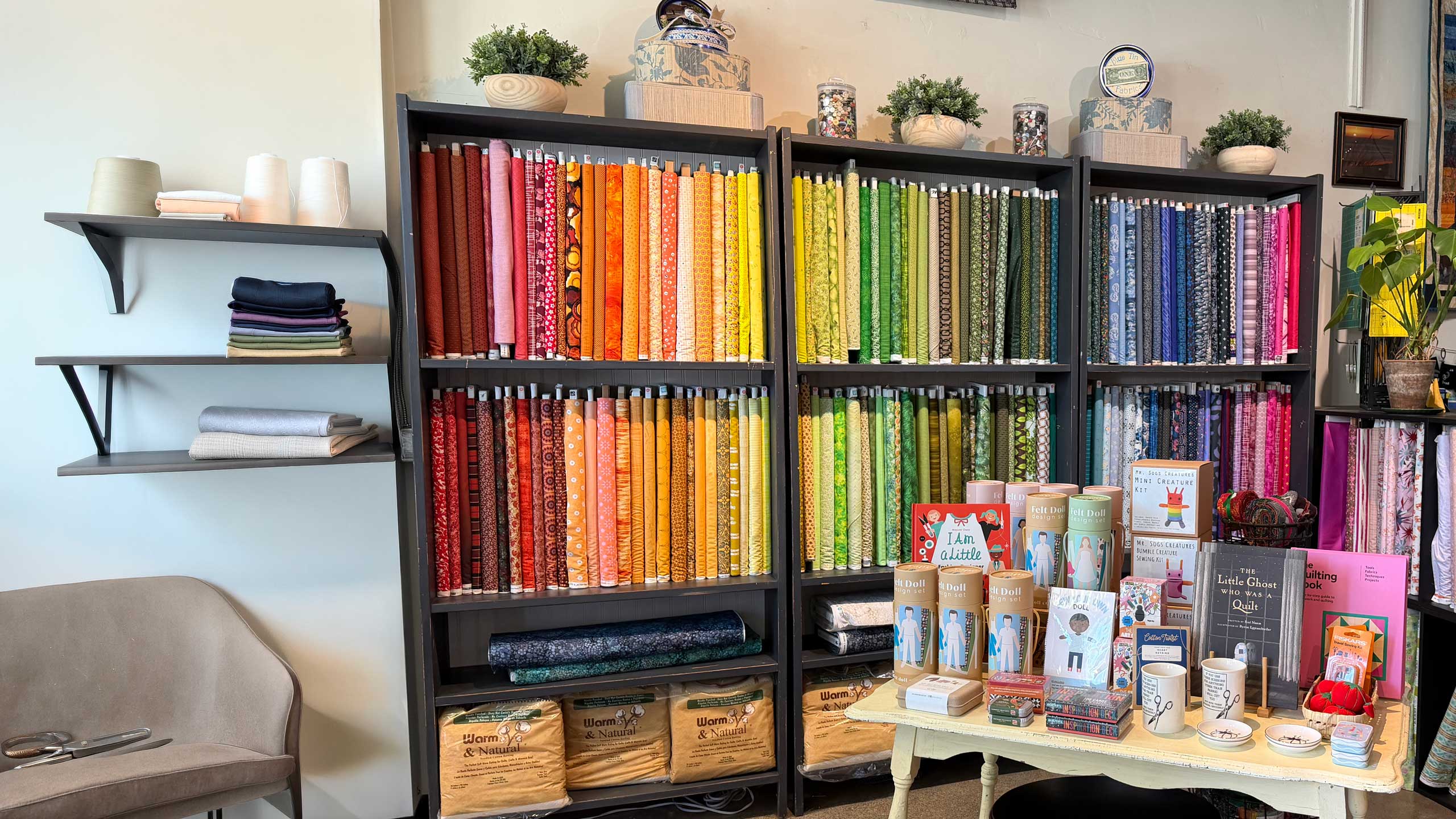 wall of shelves with bolts of fabric displayed in rainbow order